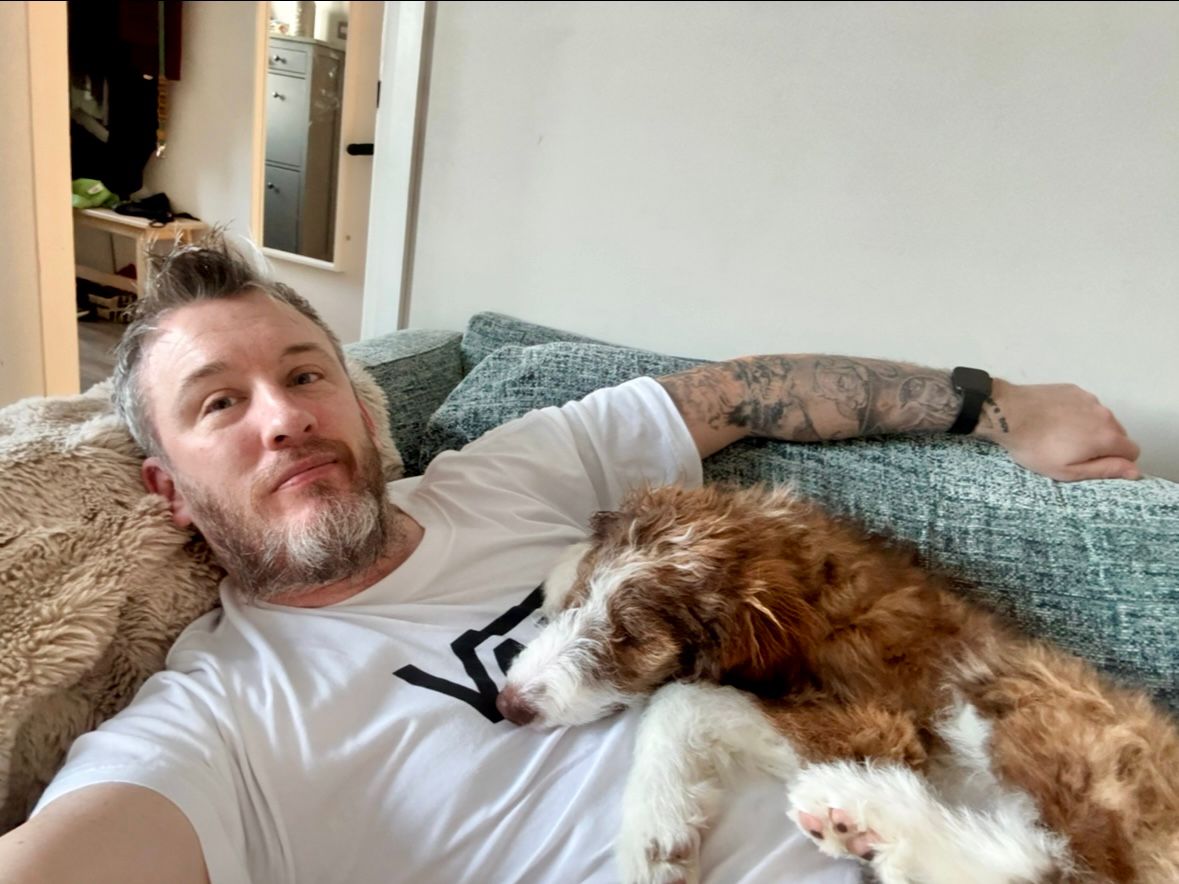 Darren relaxing at home with a dog resting beside him